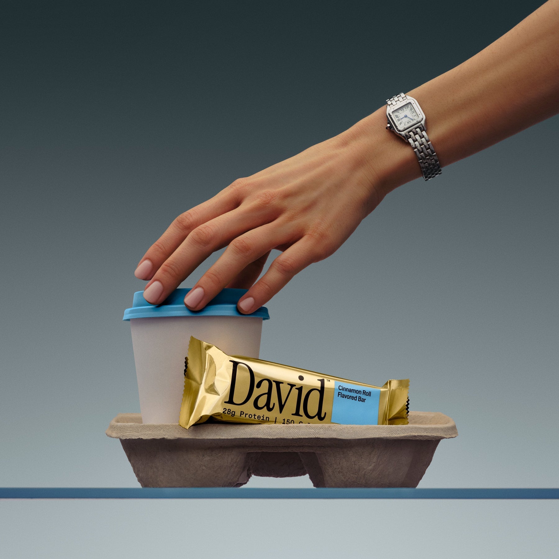 Hand reaching for a coffee cup with a David protein bar on a gray background