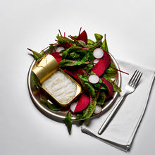 Salad with radishes and a can of cod on a white plate, accompanied by a fork and napkin.