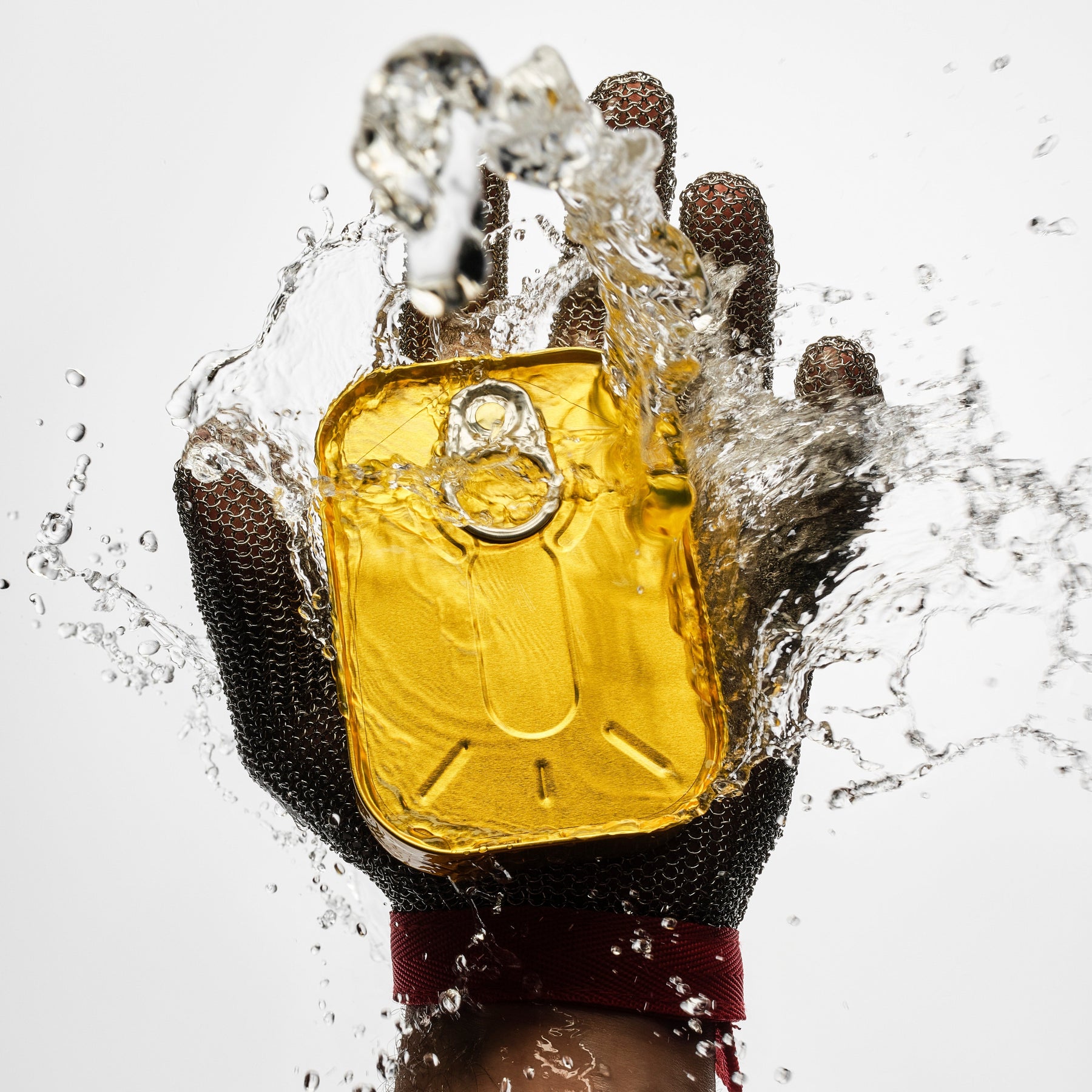 Hand wearing a silver glove holding a yellow fish can with water splashing