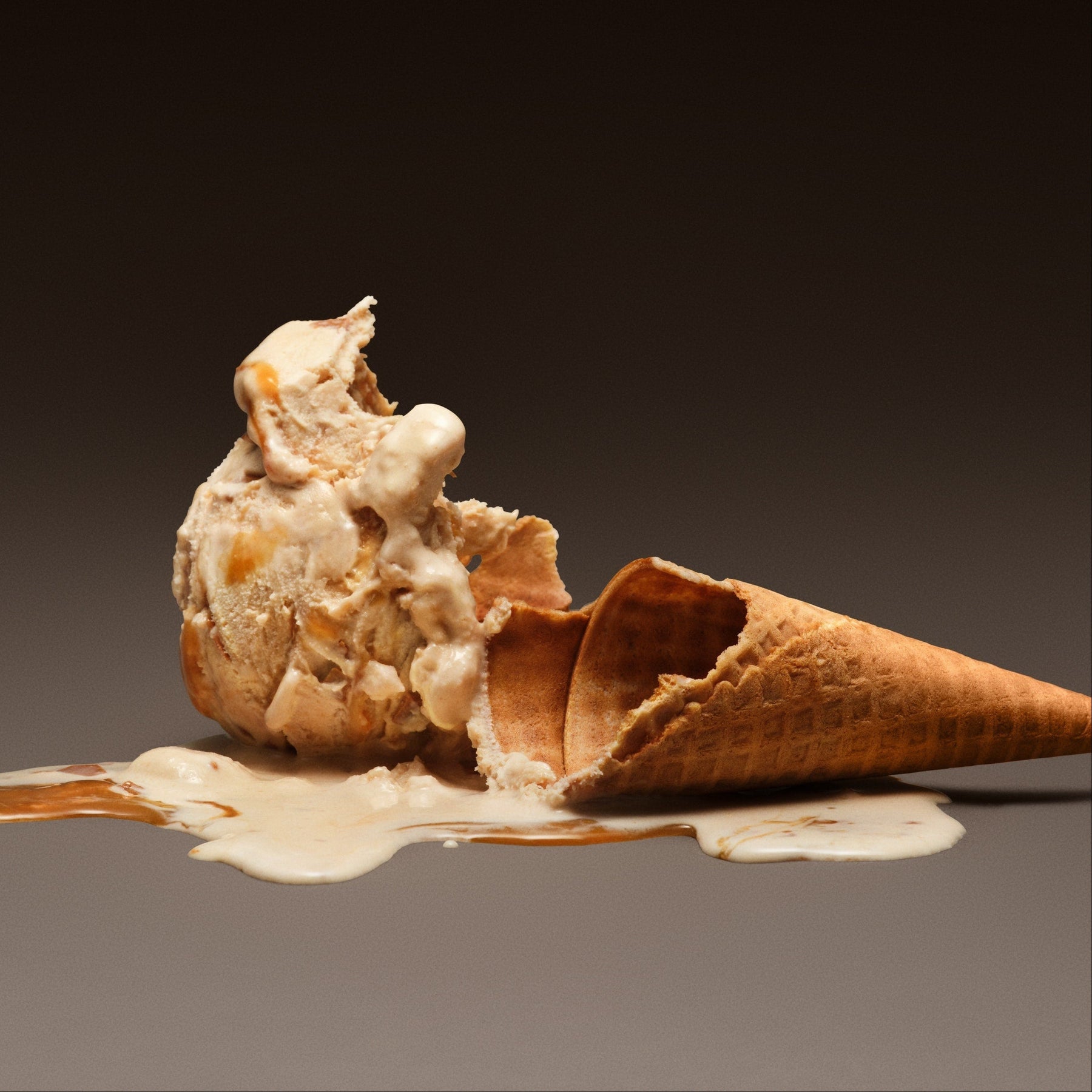 Ice cream cone with a scoop of ice cream melting on a dark background